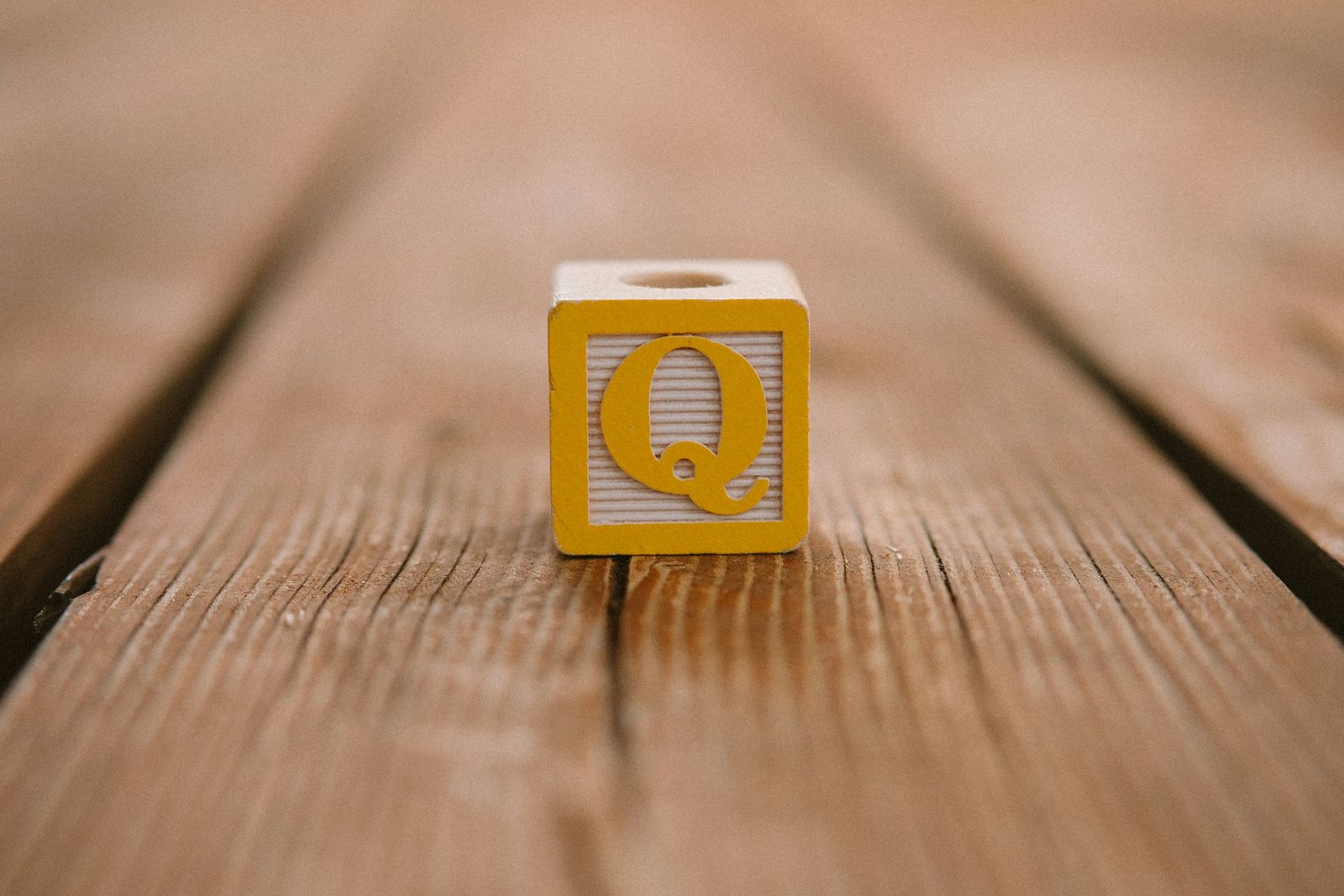 A wooden letter block showing the letter Q on a wooden table.