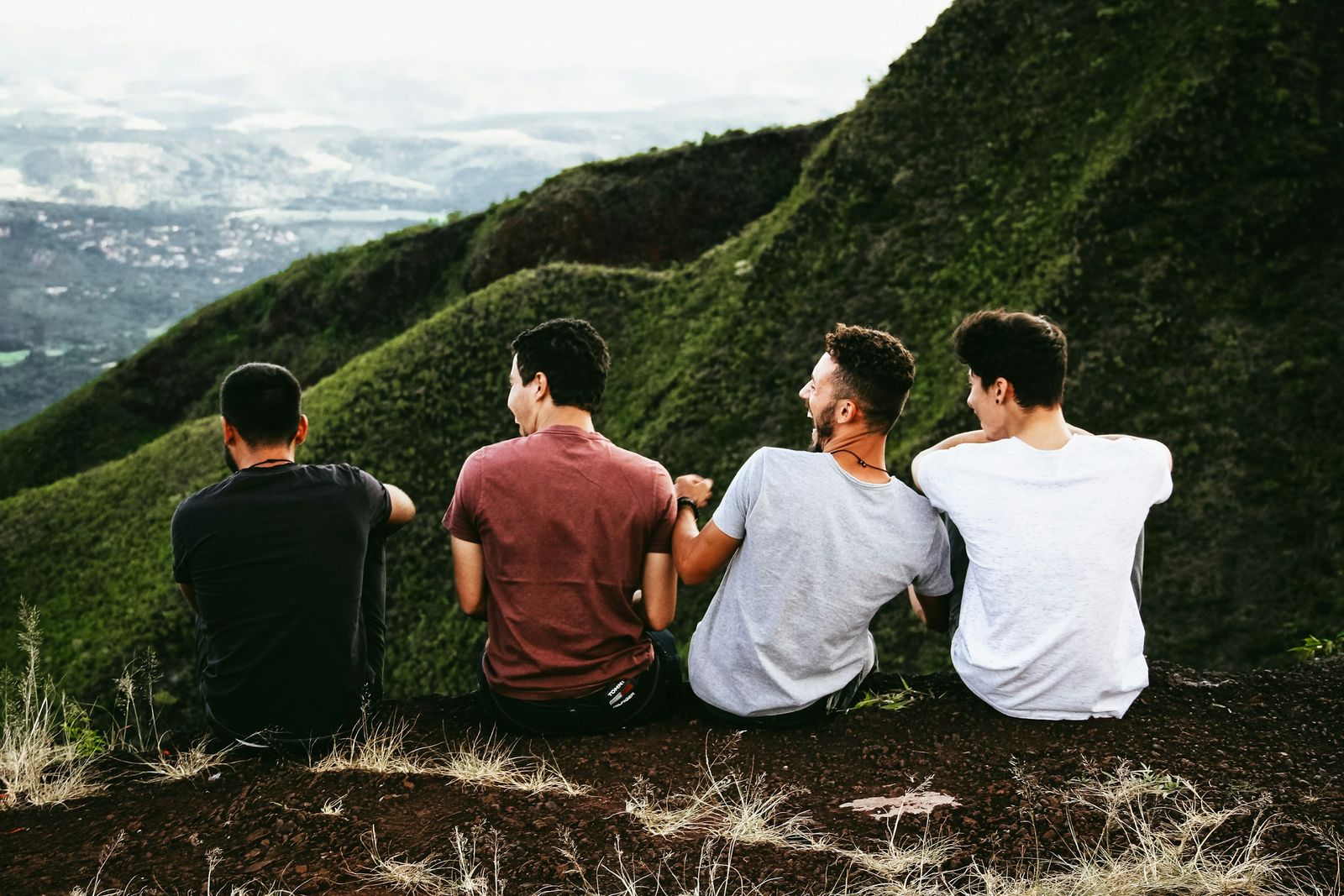 Four men sitting side by side on a hillside, looking out over the view.