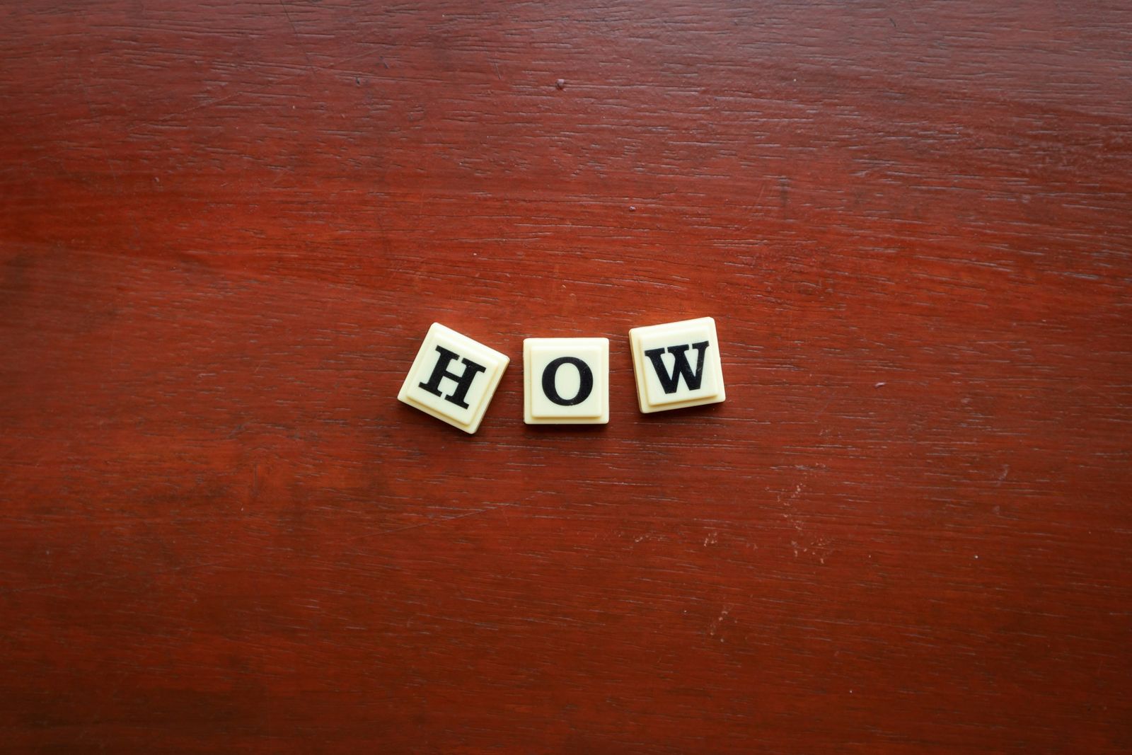 Scrabble tiles spelling the word how on a dark wooden table.