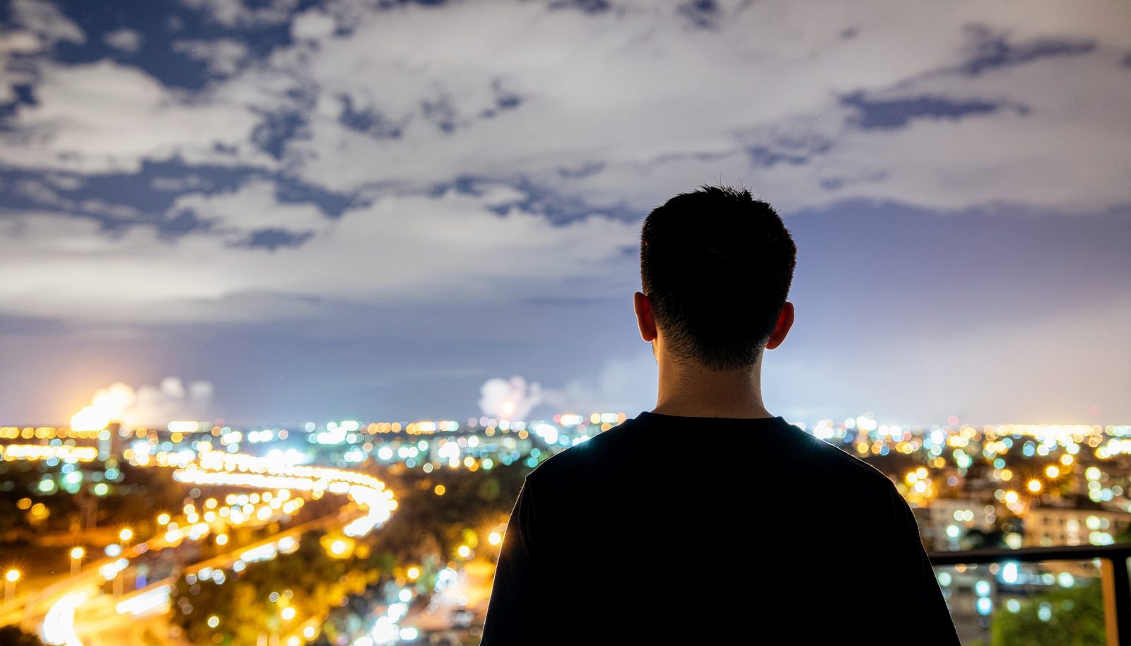 A man from behind looking out at city lights at night