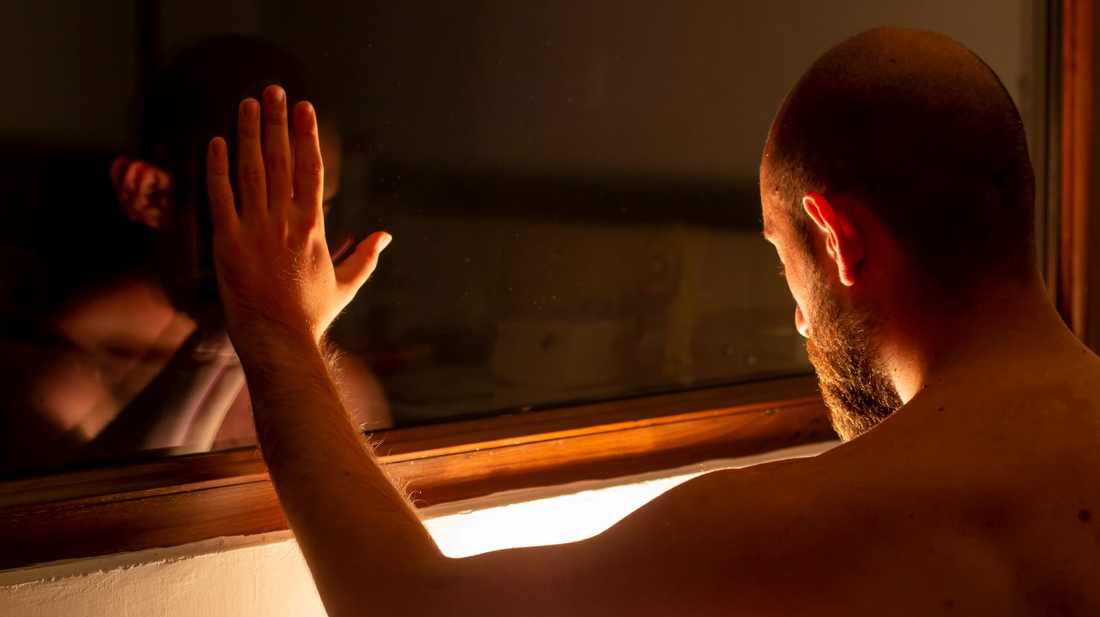 A man in silhouette by a window with his reflection